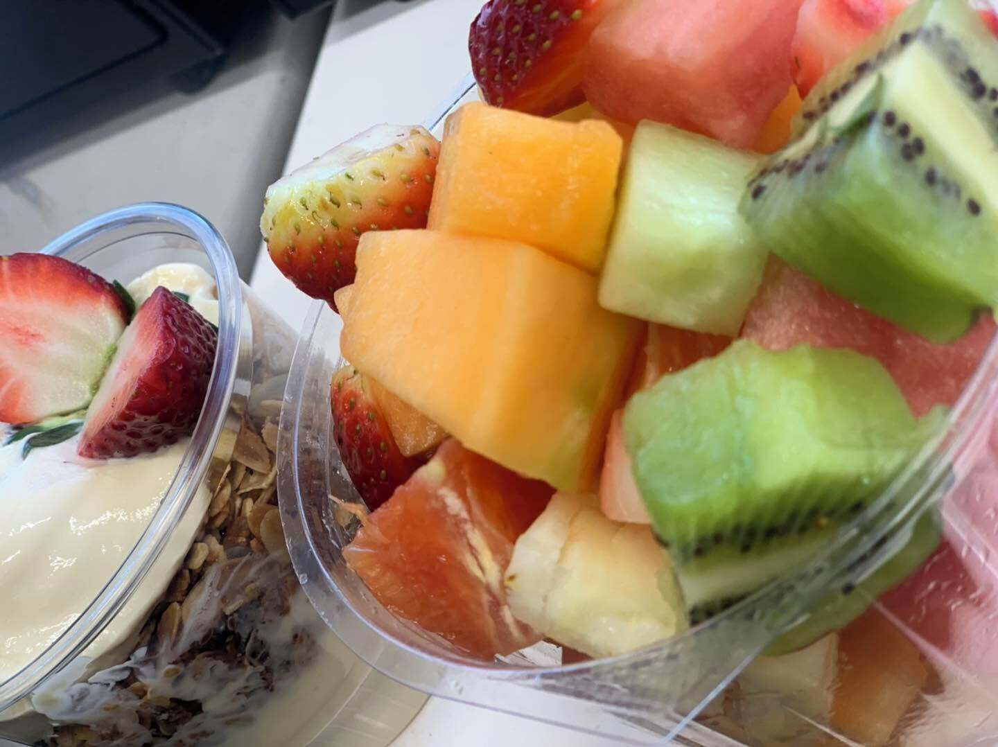 A close-up of a fruit salad with strawberries, cantaloupe, and kiwi in a clear plastic container.