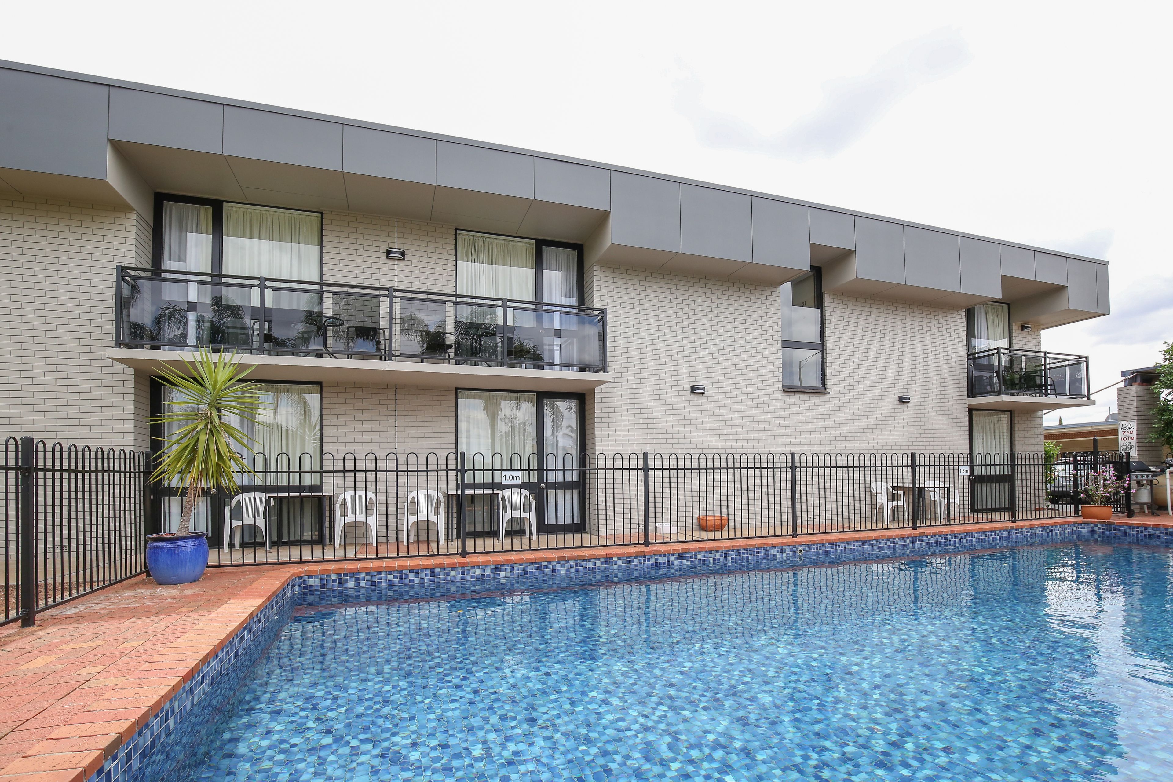 A modern building with a swimming pool, balconies, and a fenced patio area.