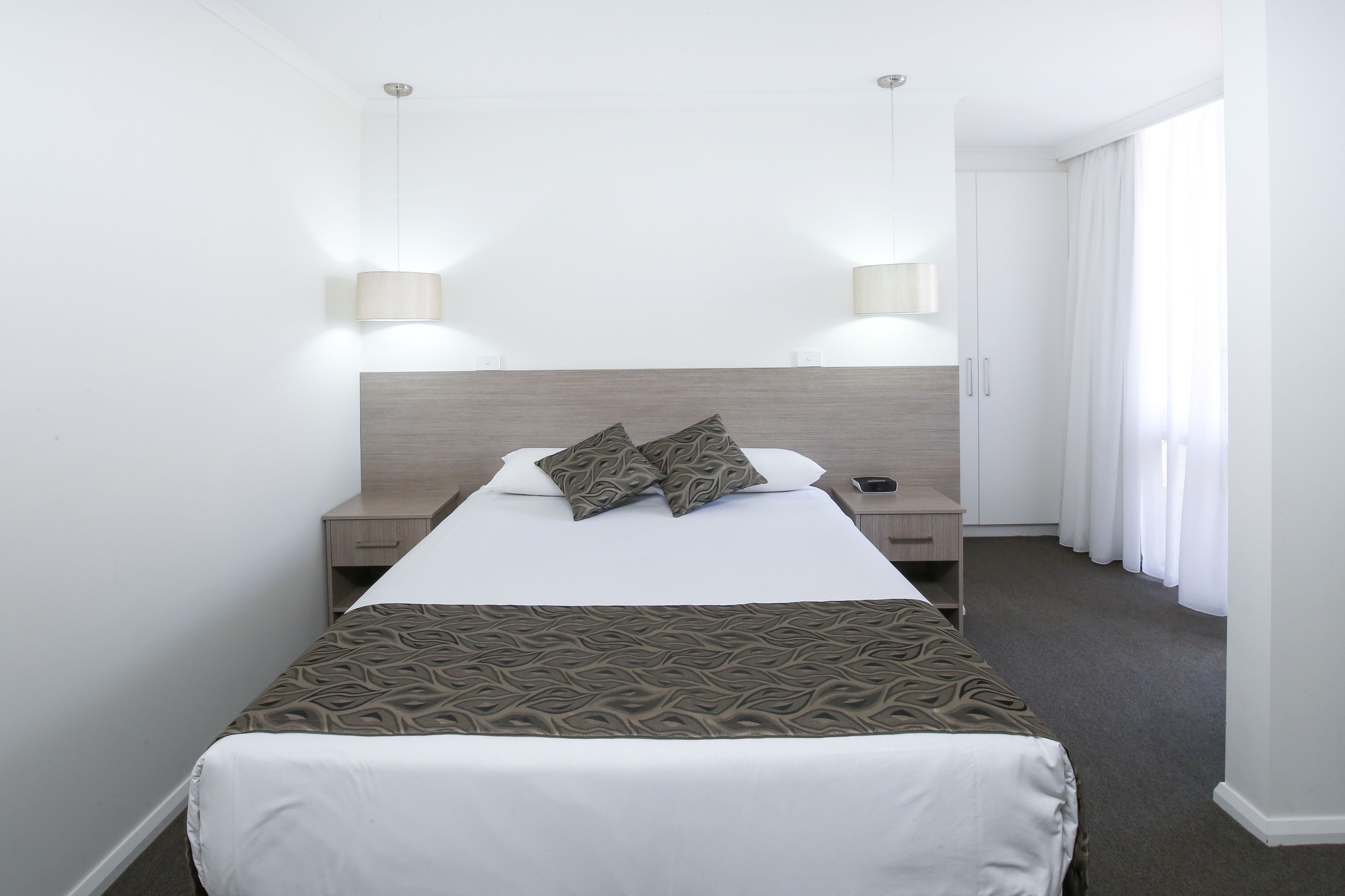 A hotel room with a bed, two bedside tables, a nightstand, a lamp, and a window with curtains.