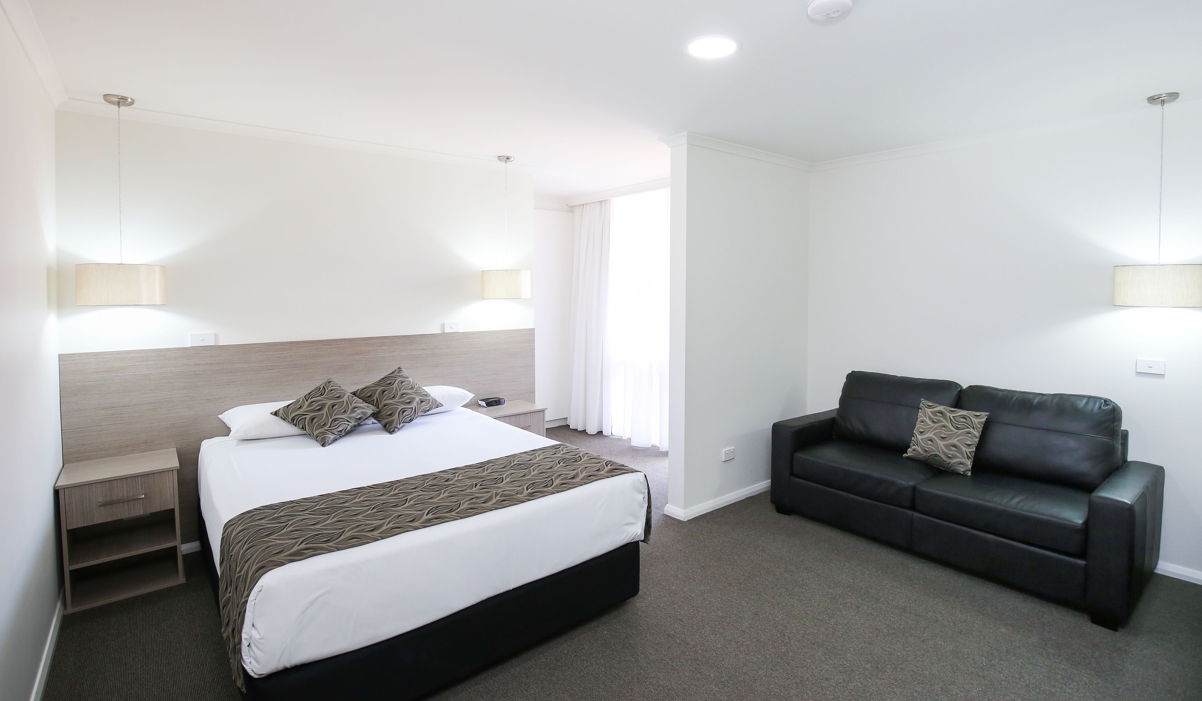 Habitación de hotel con cama, mesita de noche, lámpara y un sofá de cuero negro.