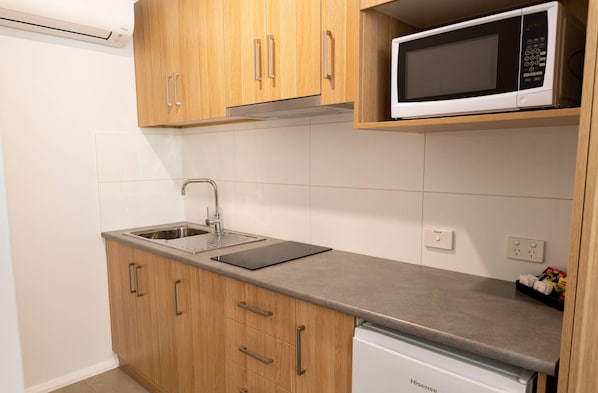 Cocina compacta con armarios de madera, un lavamanos de acero inoxidable, microondas y lavavajillas.
