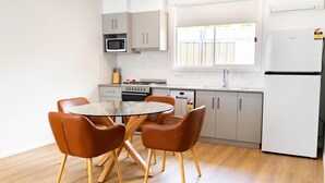 Una cocina moderna con una mesa redonda de vidrio y cuatro sillas marrones, un microondas, estufa, lavavajillas y refrigerador.