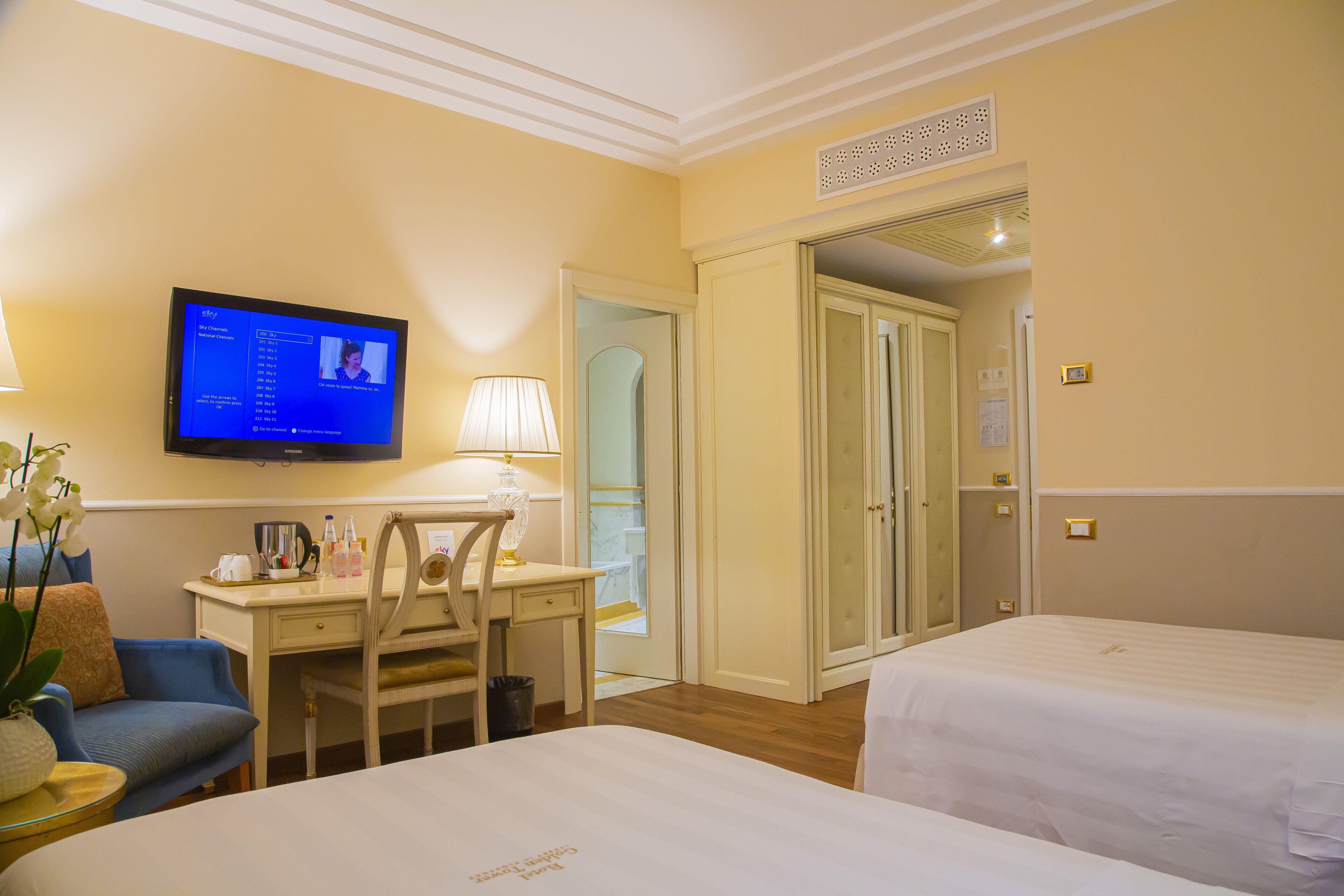 A hotel room with a bed, a desk with a chair, a television, and a door leading to a bathroom.
