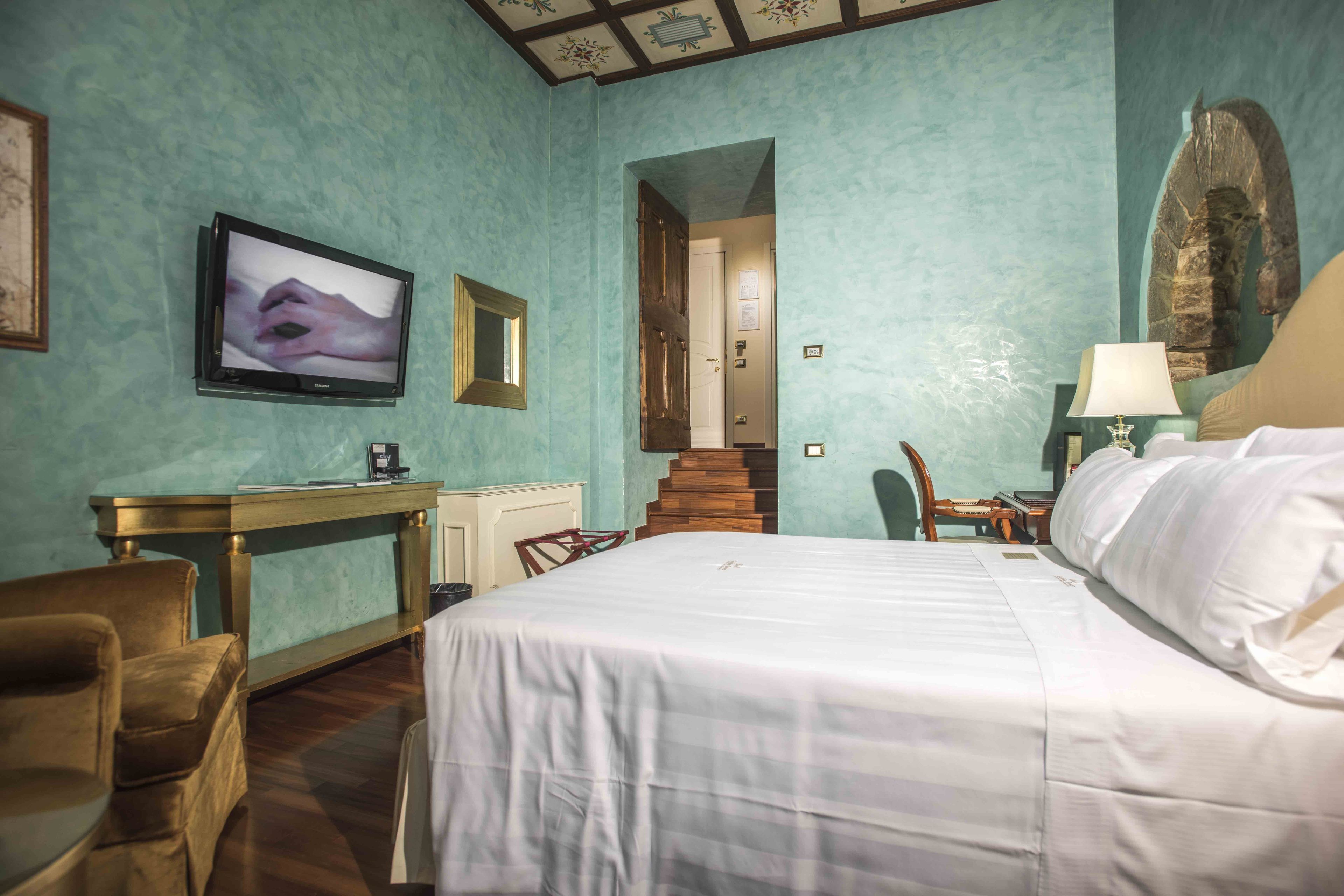 Quarto de hotel com uma cama, uma escrivaninha, uma televisão e uma cadeira.