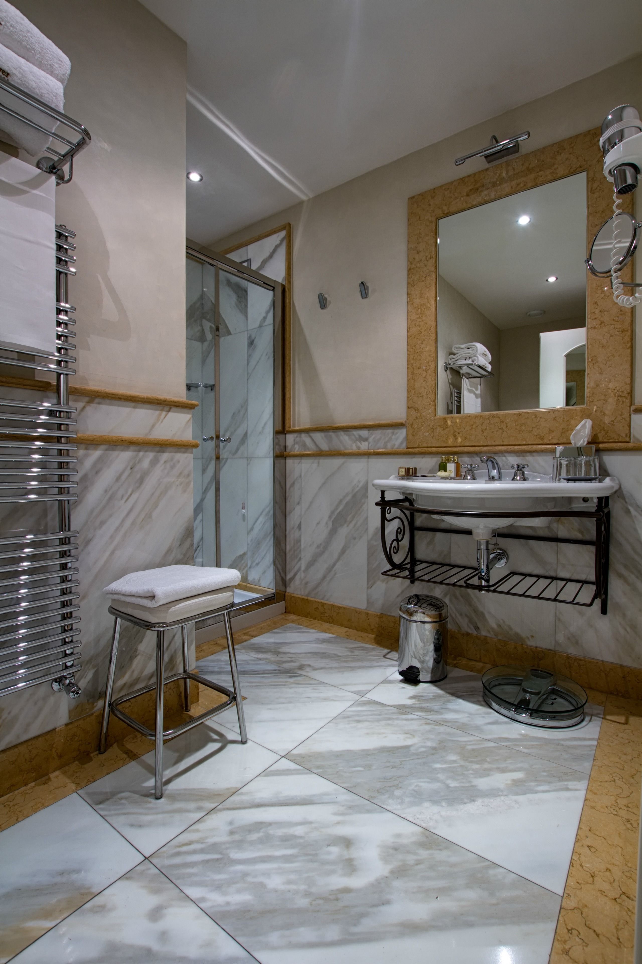 Un baño con piso de mármol, un lavamanos blanco, un espejo grande y una cabina de ducha con paredes de vidrio.