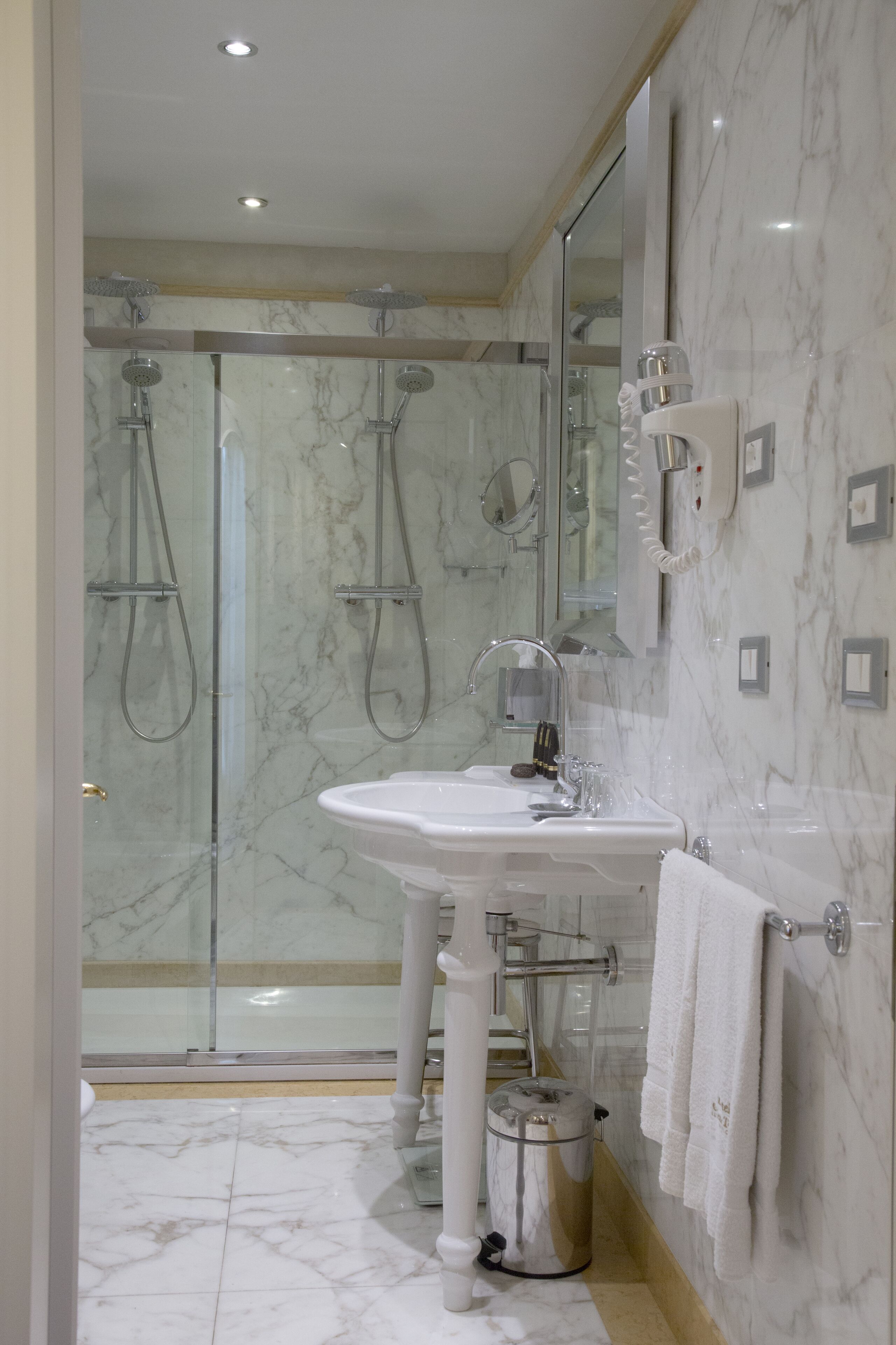Un bagno moderno con doccia vetrata, lavandino bianco e pavimento in marmo.