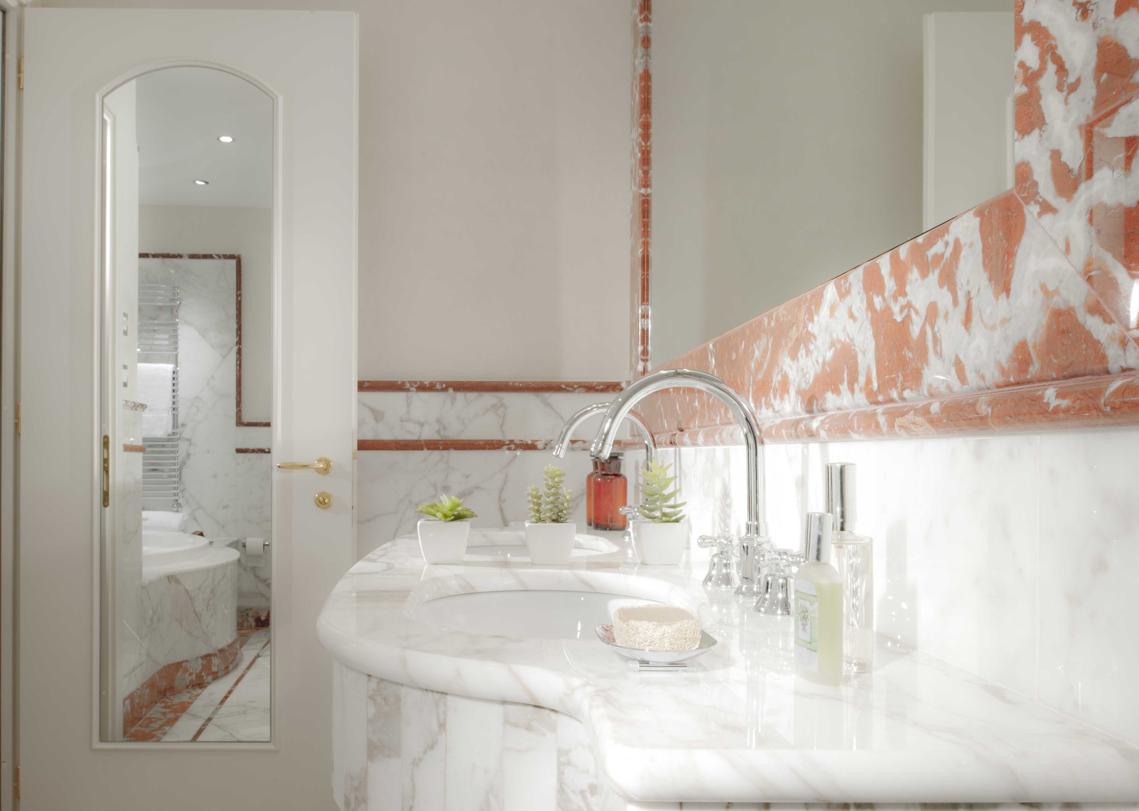 A bathroom with a marble sink, a large mirror, and a door leading to another room.
