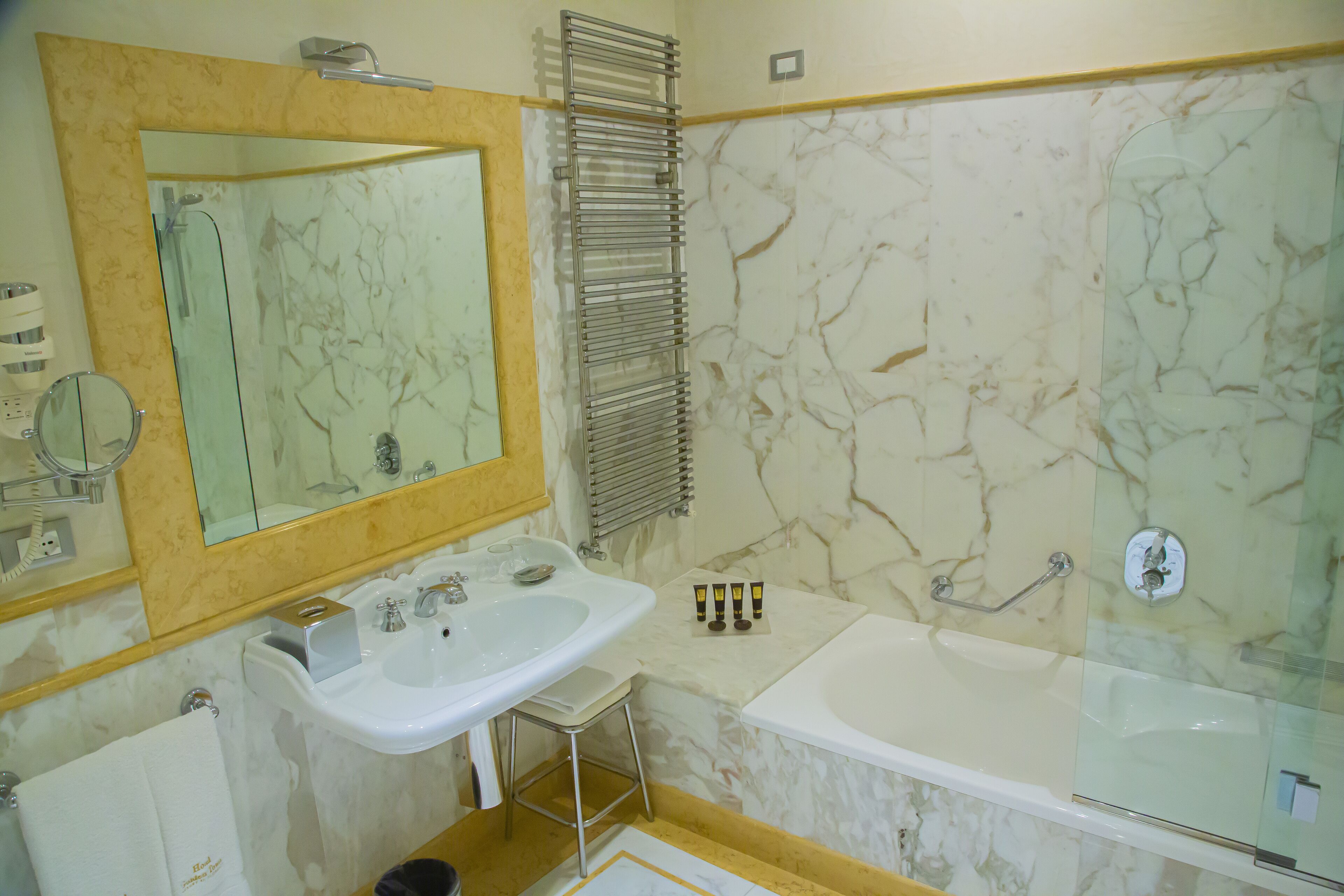 A bathroom with a marble wall, a sink, a bathtub, and a mirror.