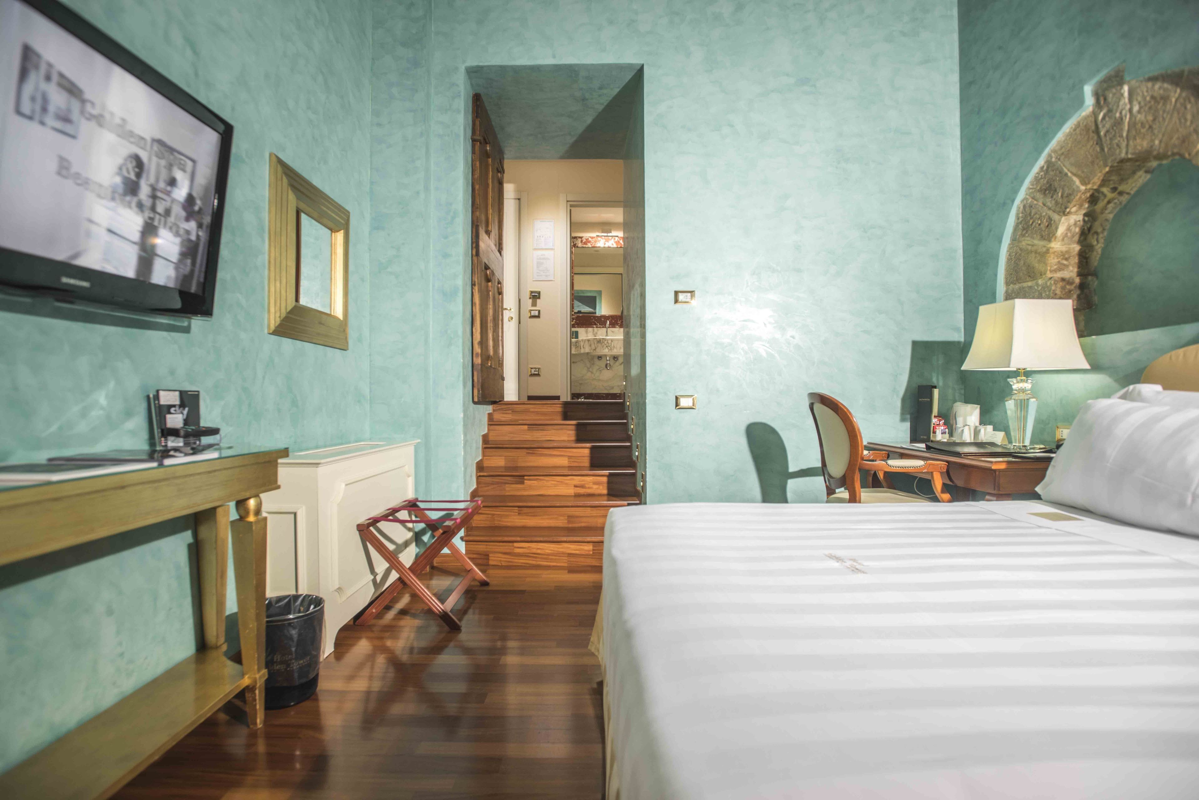 A hotel room with a bed, desk, chair, and a television on the wall.