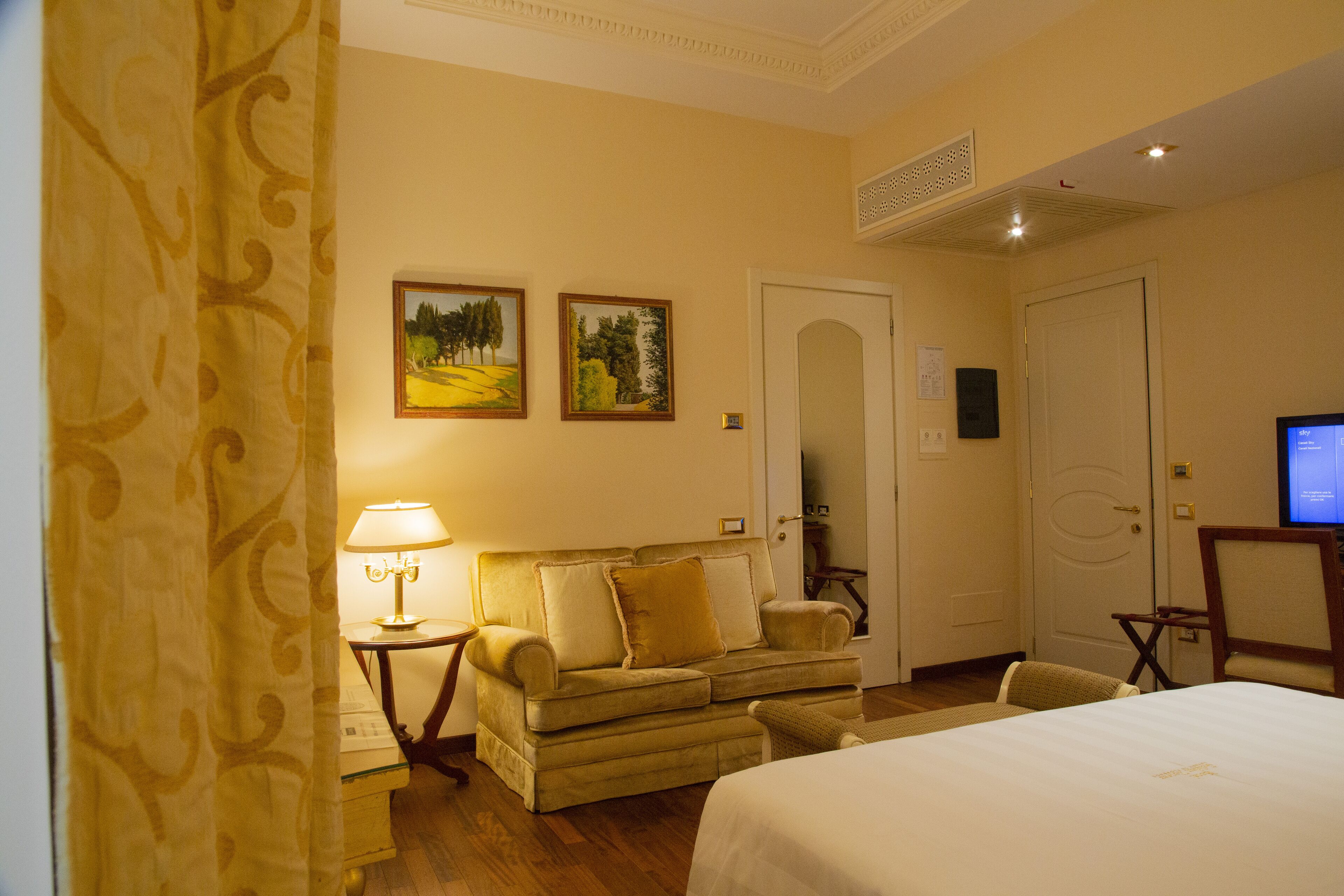 Quarto de hotel com uma cama, um sofá, uma televisão e duas pinturas na parede.