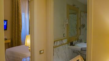Une chambre d’hôtel comprenant un lit, une table de chevet avec une lampe, une salle de bain avec un miroir, un lavabo et une chaise.