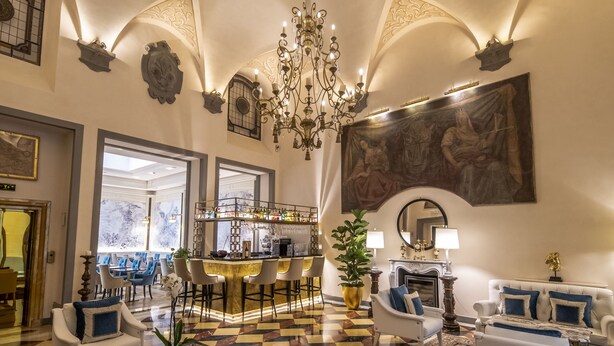 A spacious lobby with a checkered floor, a bar area, seating arrangements, and a large painting on the wall.
