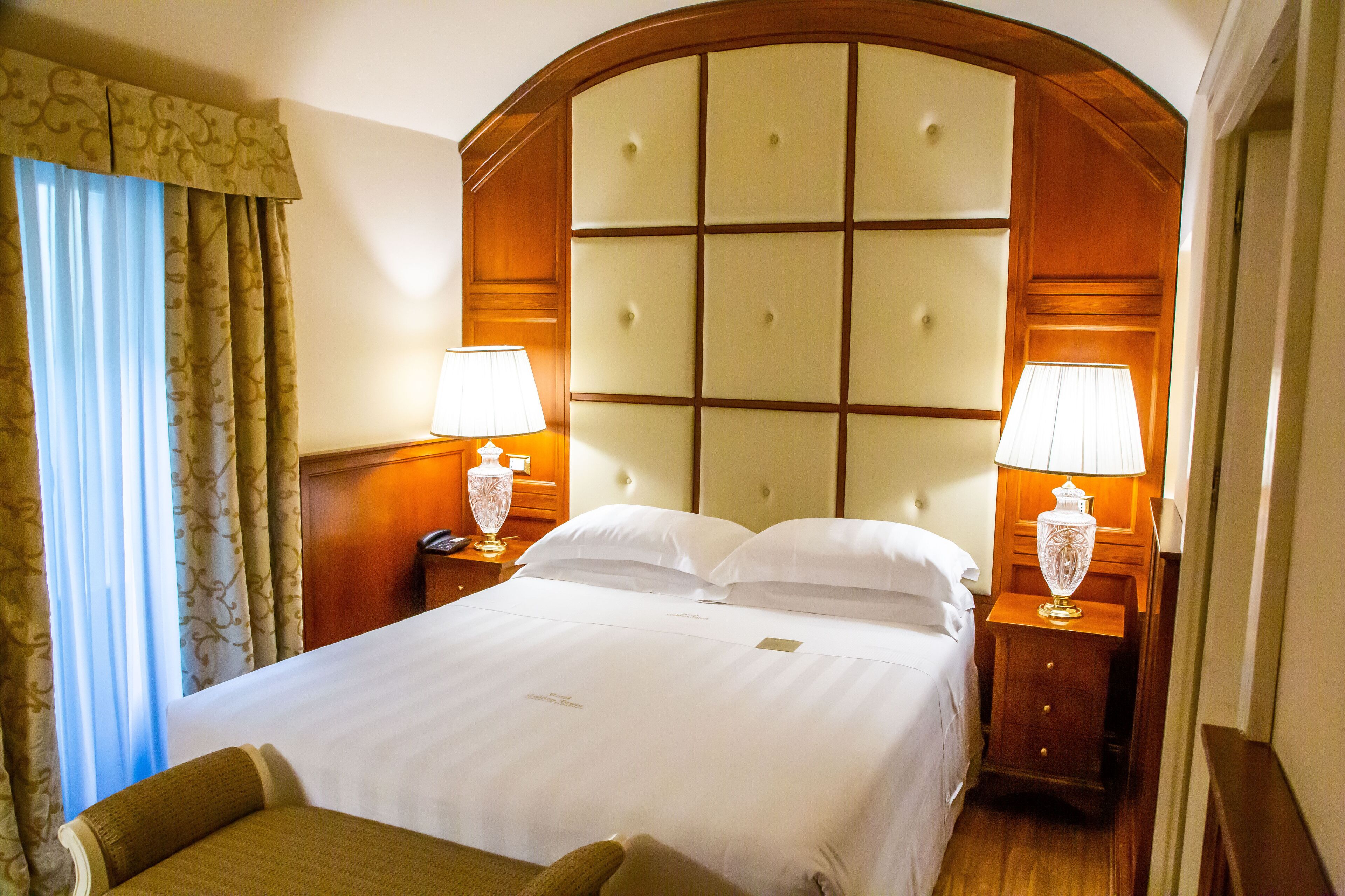 Una habitación de hotel con una cama grande, dos mesitas de noche con lámparas y un cabecero de madera.