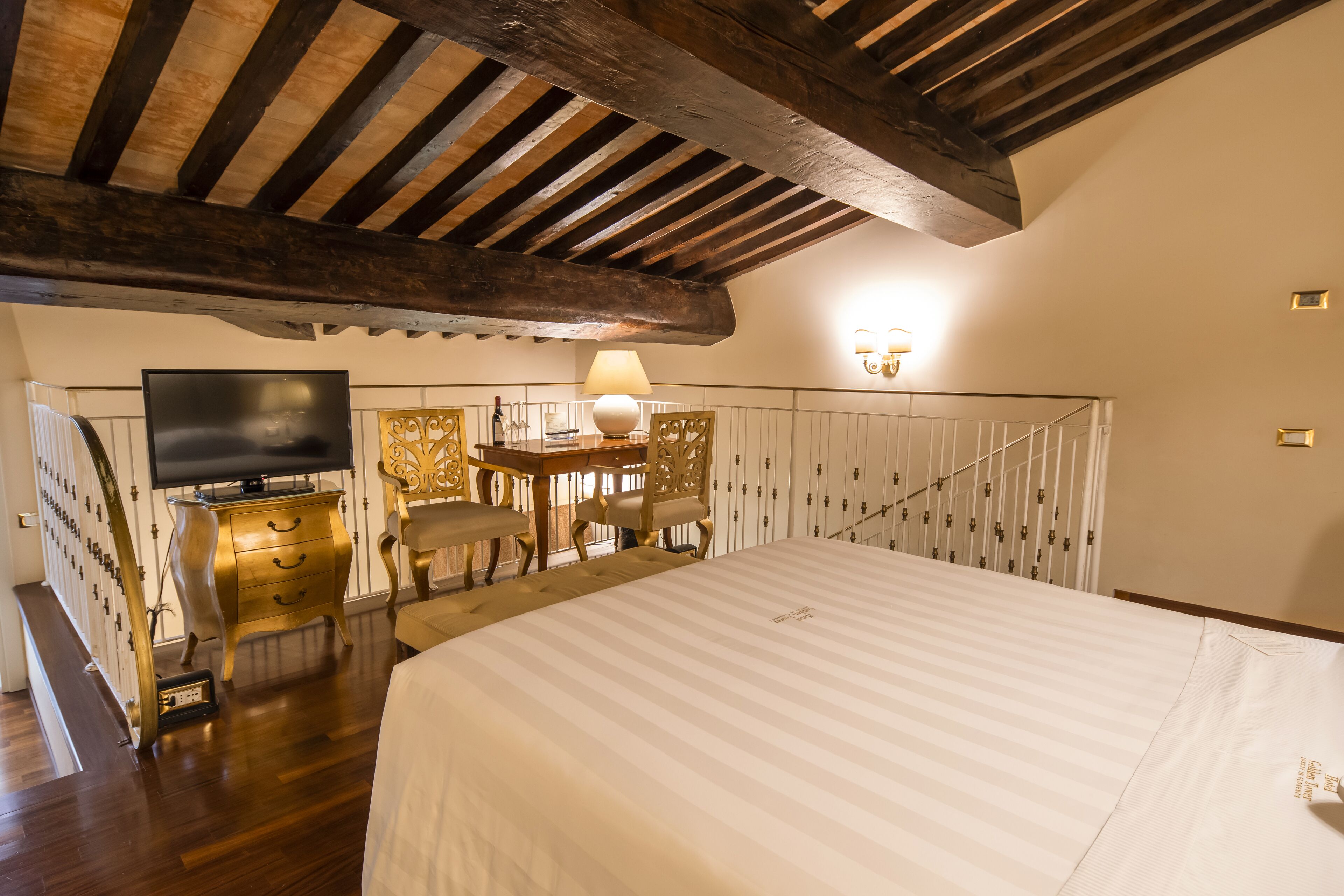 Una habitación de hotel con una cama grande, televisión, escritorio con lámpara y una escalera.