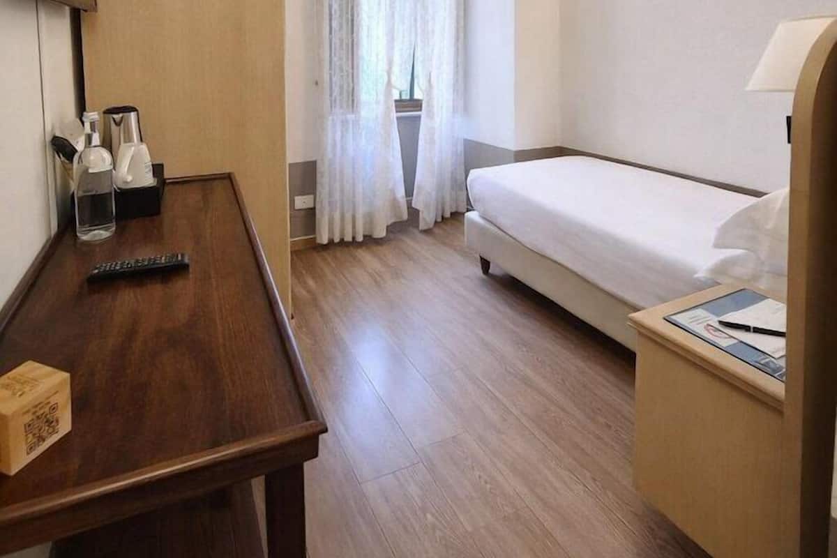 Une chambre d’hôtel avec un bureau en bois, un lit, une télévision et une lampe fixée au mur.