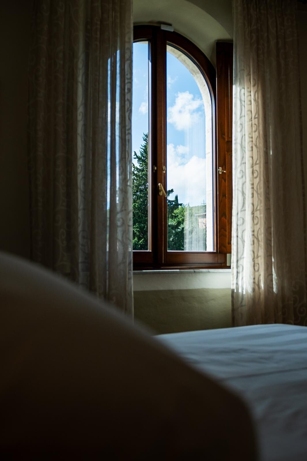 A bedroom with a large window, curtains, and a bed.
