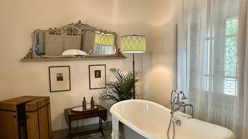 Un baño con una bañera independiente, una araña, un espejo con marco decorativo y un suelo de patrón hexagonal.