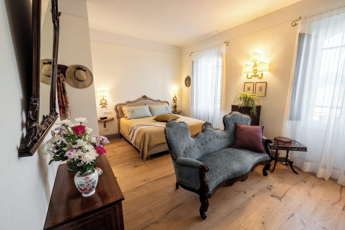 Une chambre à coucher avec un lit, une chaise, une table de chevet, une lampe et un miroir.