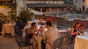 Un espacio de comedor al aire libre con mesas y sillas, un muro de piedra y un río al fondo.
