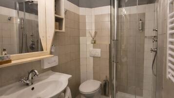 Un baño moderno con dos lavamanos, un inodoro y ducha con mampara de vidrio.