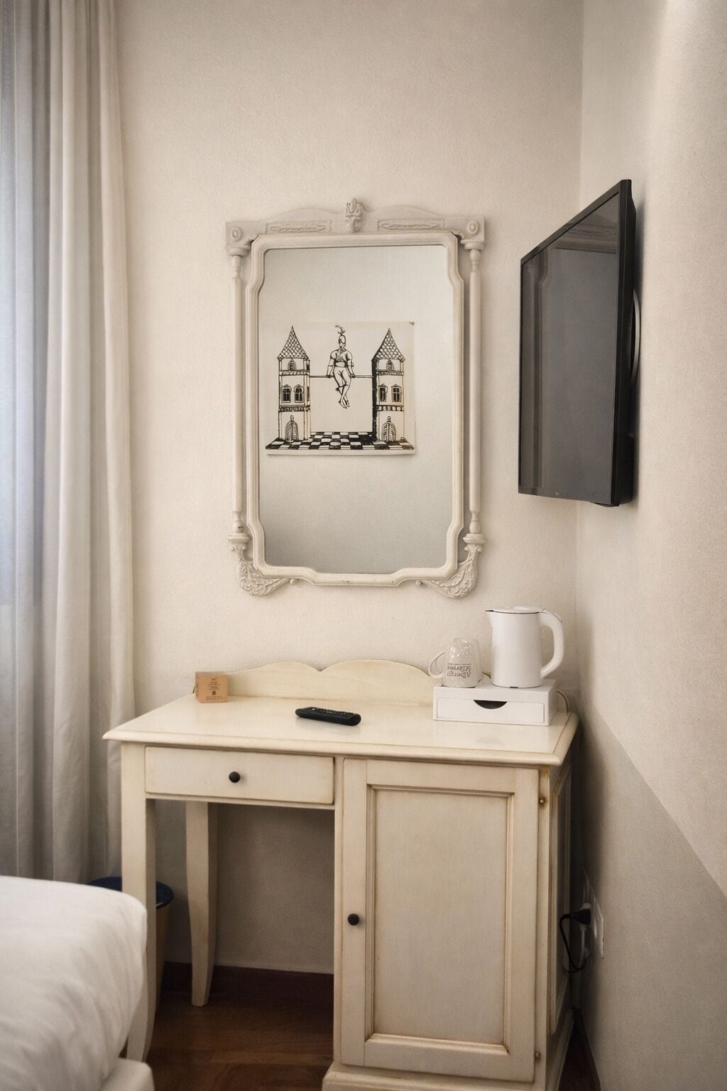 Habitación de hotel con un escritorio blanco, una obra de arte enmarcada de un castillo, un televisor de pantalla plana y una cafetera.