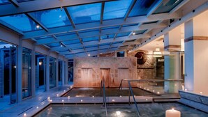 Un área de spa con hidromasaje, paredes de vidrio y una pared de piedra con un reloj.