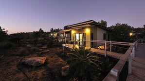 A modern building with a wooden deck and a bridge, surrounded by rocks and sparse vegetation.