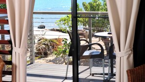 A balcony with a view of the sea, featuring a table and chairs, and a wicker chair inside.