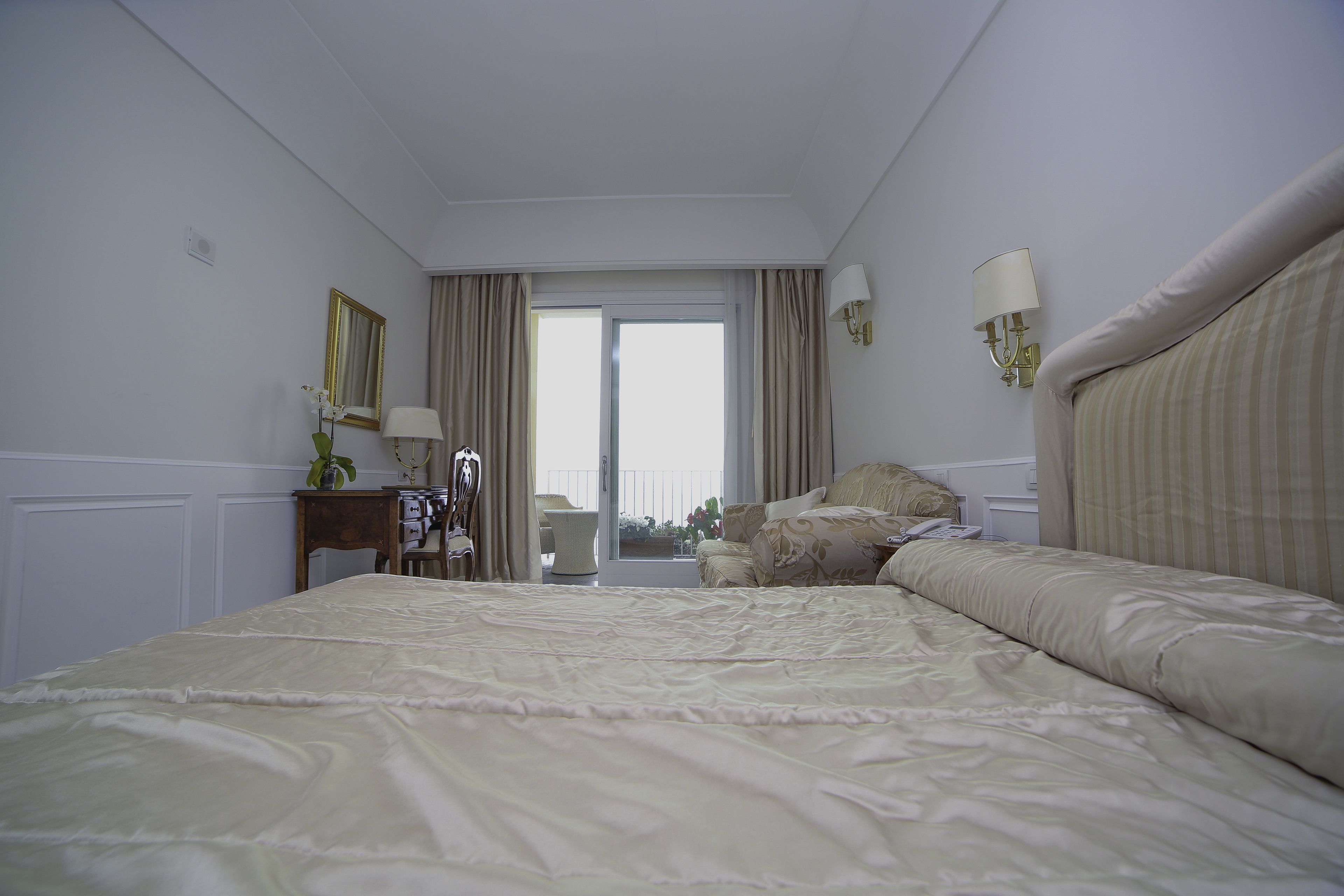A hotel room with a large bed, a desk with a lamp, a chair, and a view through a glass door.