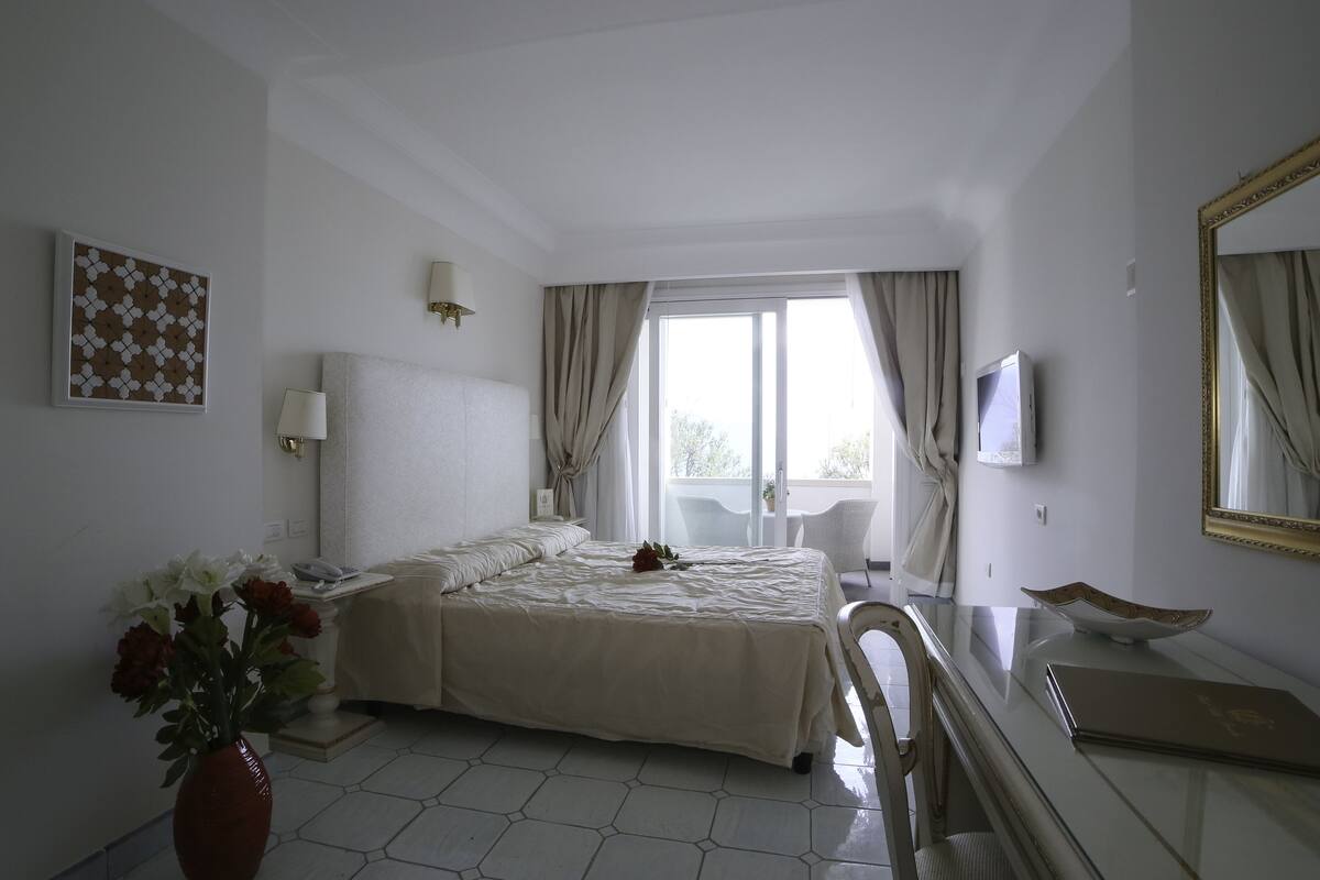 A bedroom with a bed, bedside table, lamp, and a large mirror.