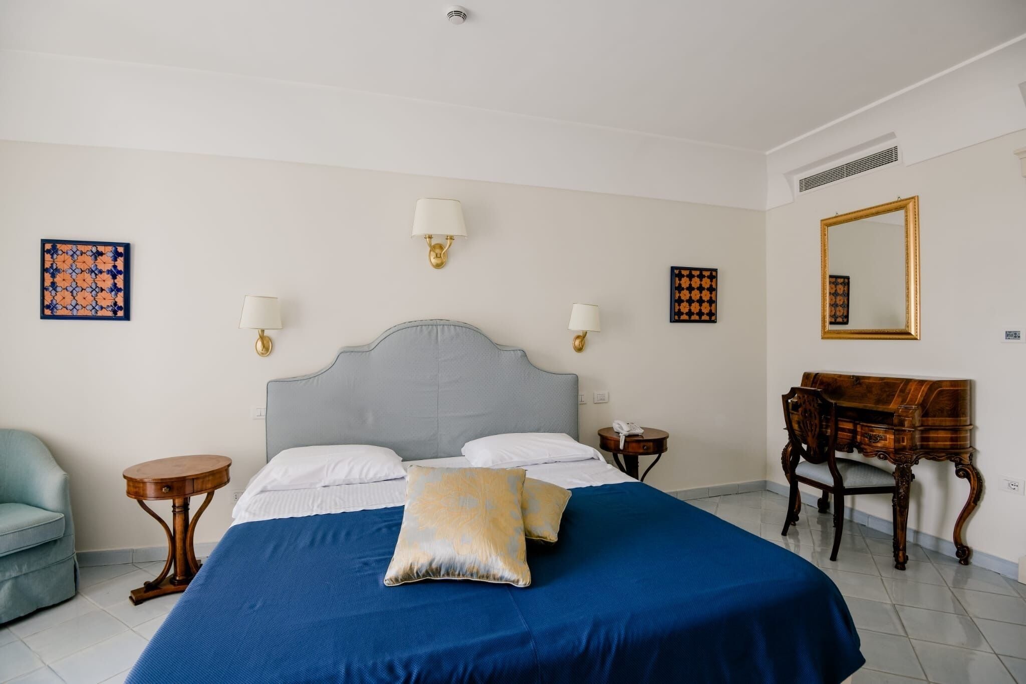 A bedroom with a bed, bedside tables, a chair, a desk, and a mirror.