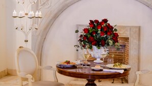 Un coin repas avec une table dressée pour deux personnes, un lustre et une cheminée ornée d’une fresque représentant des oiseaux.