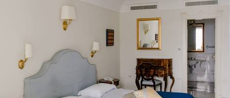 A hotel room with a bed, bedside lamps, a mirror, a wooden dresser, and a bathroom visible through an open door.