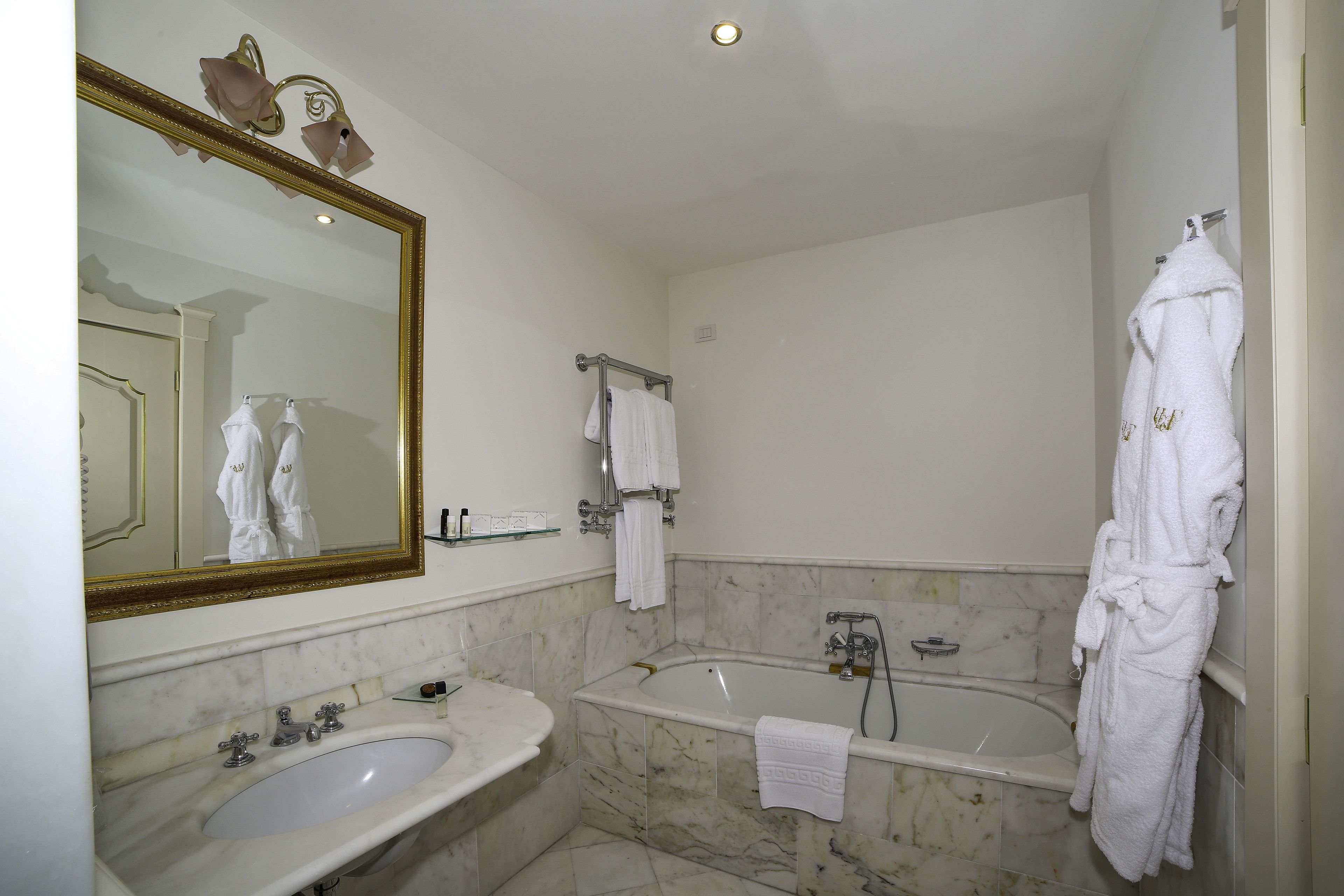 A bathroom with a marble sink, a bathtub, and a large mirror.