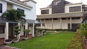 Un patio con césped verde, plantas en macetas y una zona de estar cubierta.