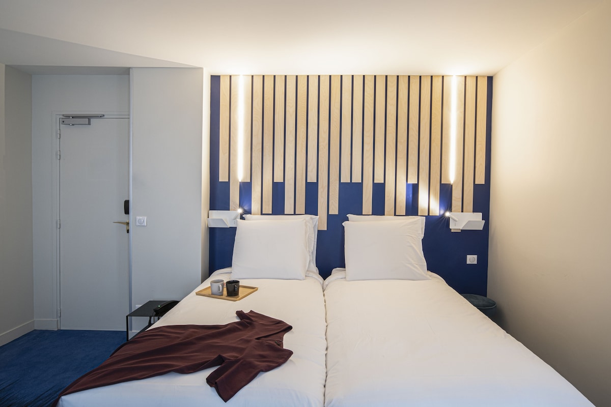 A hotel room with two beds, a wooden headboard, bedside tables, and a door.