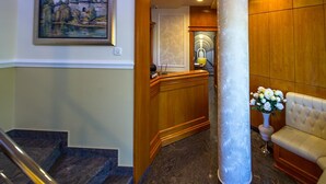A hotel lobby with a staircase, a reception desk, a seating area, and a painting on the wall. - Cezar Hotel (Banja Luka)