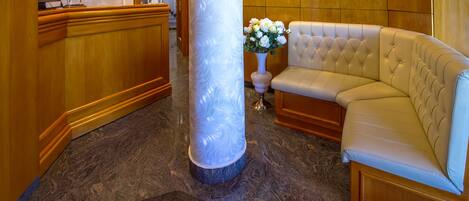 A lobby with a marble floor, a reception desk, a large white pillar, a tufted leather sofa, and a vase of flowers.