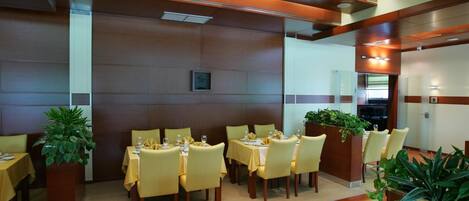 A restaurant with tables set for dining, wooden paneling on the walls, and potted plants.