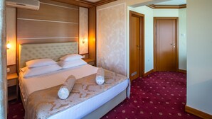 A hotel room with a large bed, bedside lamps, a wooden headboard, and a red carpeted floor. - Cezar Hotel (Banja Luka)