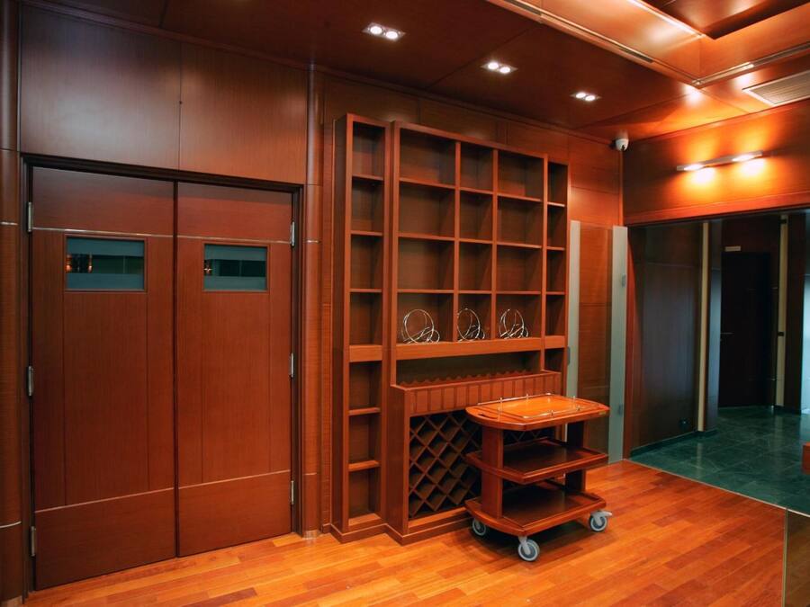A wooden interior with a sliding door, built-in shelves, and a wheeled cart.