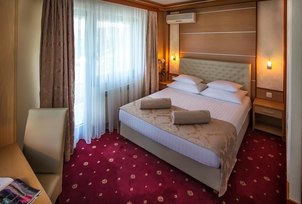 A hotel room with a large bed, a chair, a nightstand, and a window with curtains.