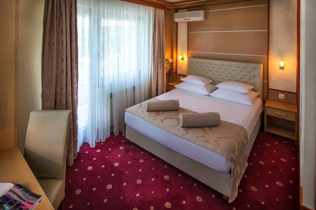 A hotel room with a large bed, a chair, a nightstand, and a window with curtains.
