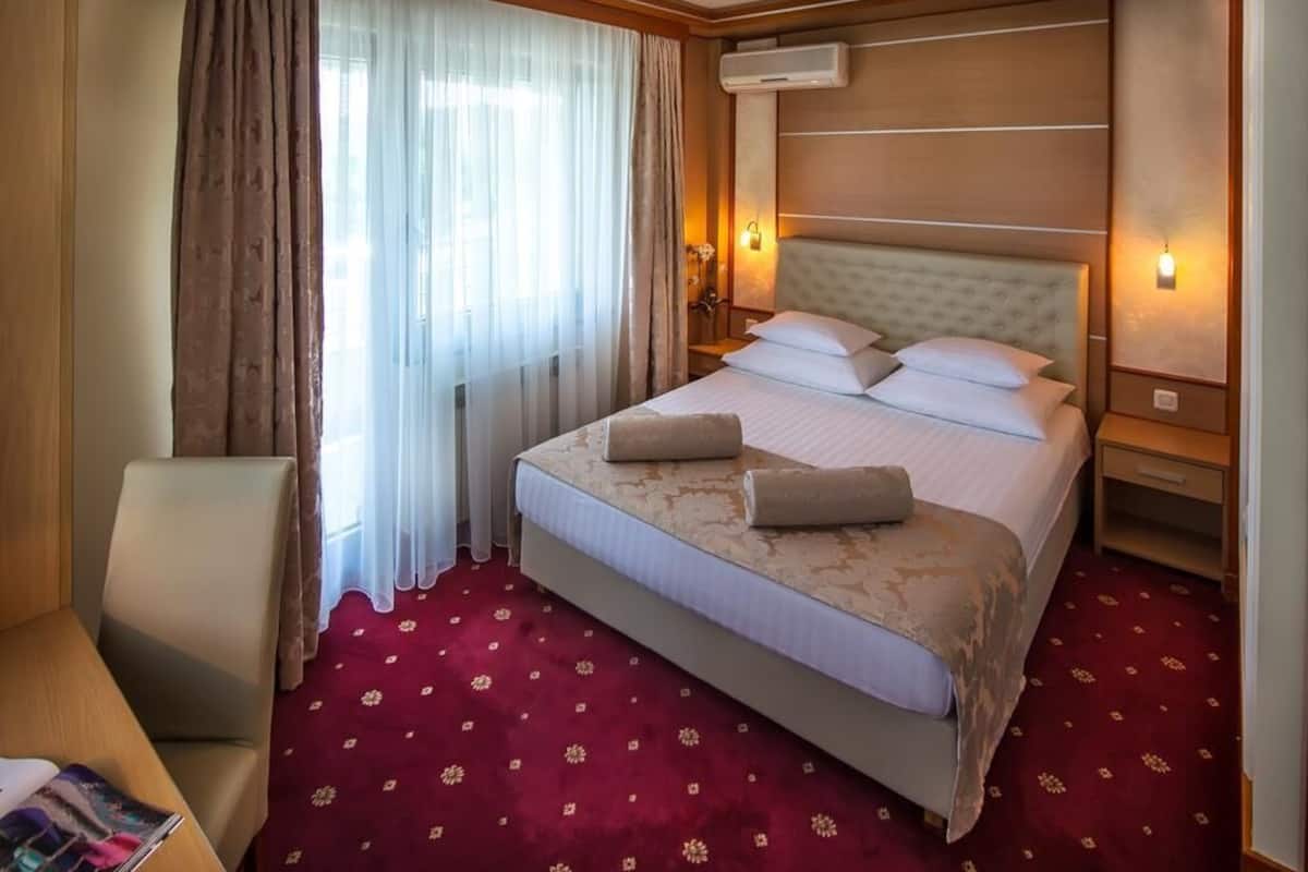Une chambre d’hôtel avec un grand lit, une chaise, une table de chevet et une fenêtre avec des rideaux.