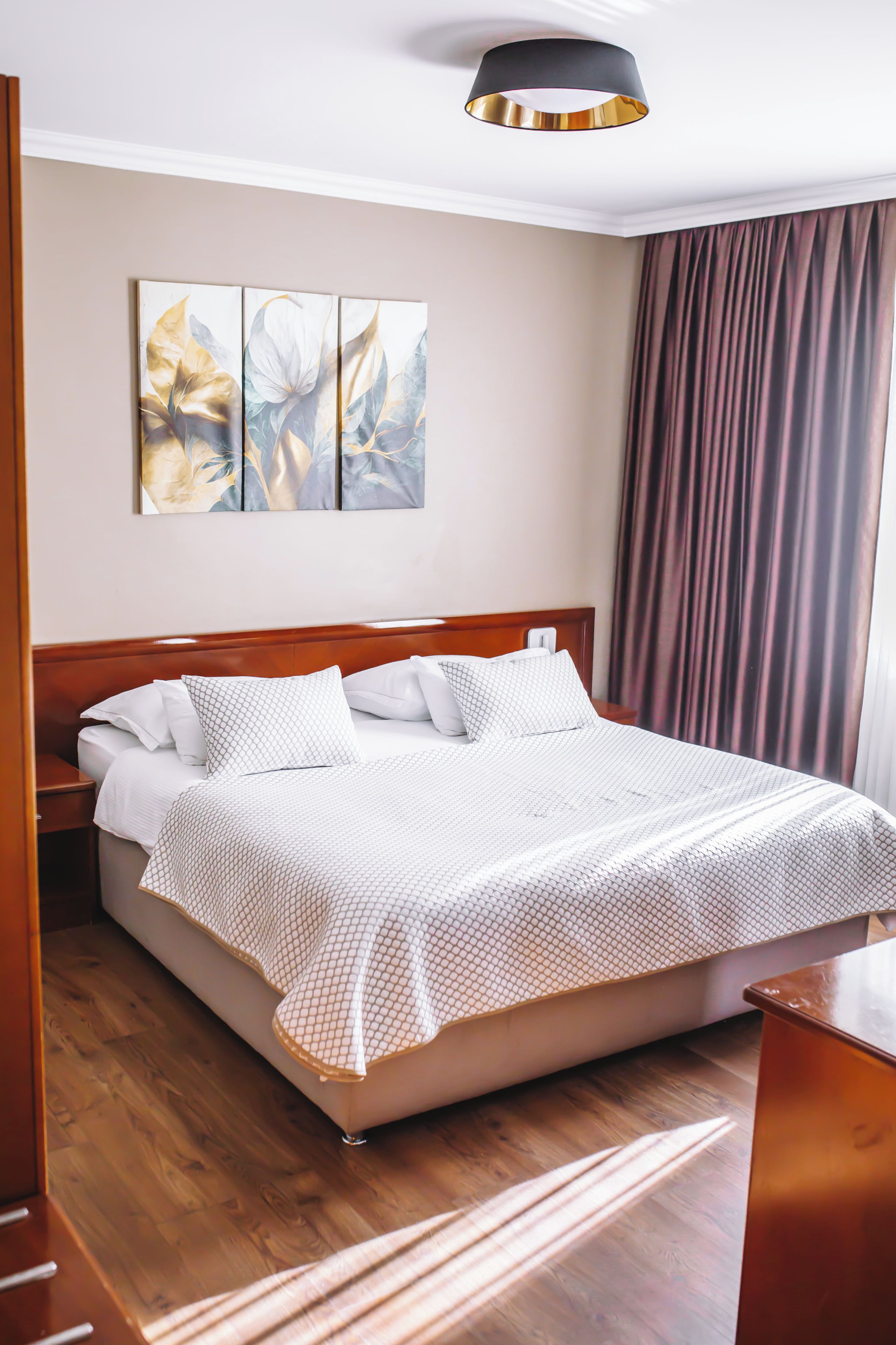 Ein ordentlich gemachtes Bett mit weißer, gemusterter Bettdecke, einem hölzernen Kopfteil und einem an der Wand hängenden Kunstwerk.