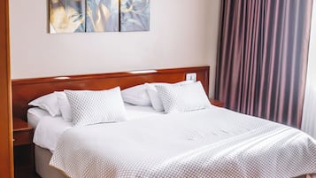 A neatly made bed with a white and patterned bedspread, a wooden headboard, and a wall-mounted artwork above.