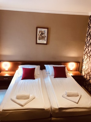 A double room with two beds, each with a pillow and a folded towel. There is a framed picture on the wall and a patterned curtain. - Bristol (Mostar)