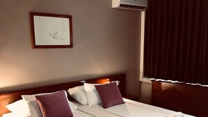 A hotel room with two beds, a framed picture on the wall, an air conditioning unit, and a window with curtains. - Bristol (Mostar)