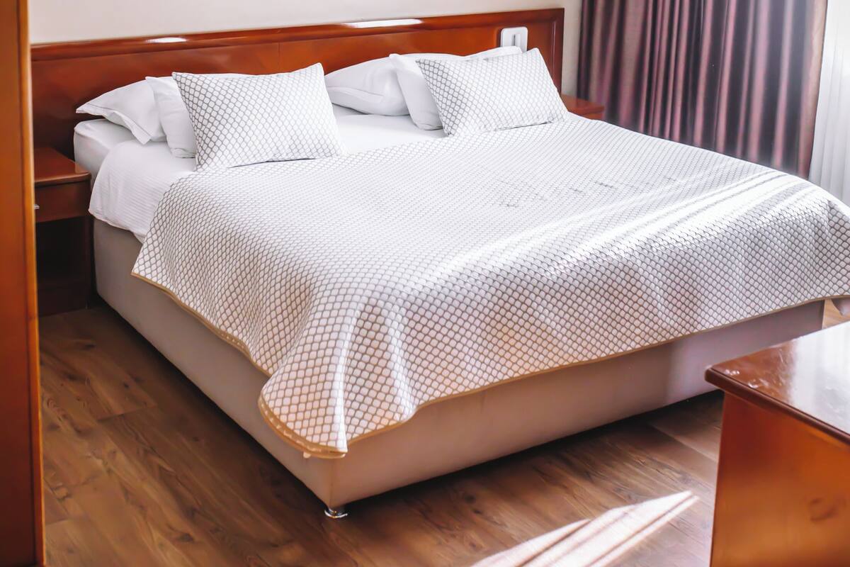 Een netjes opgemaakt bed met een wit en patroon beddegoed, een houten hoofdbord en een wanddecoratie erboven.