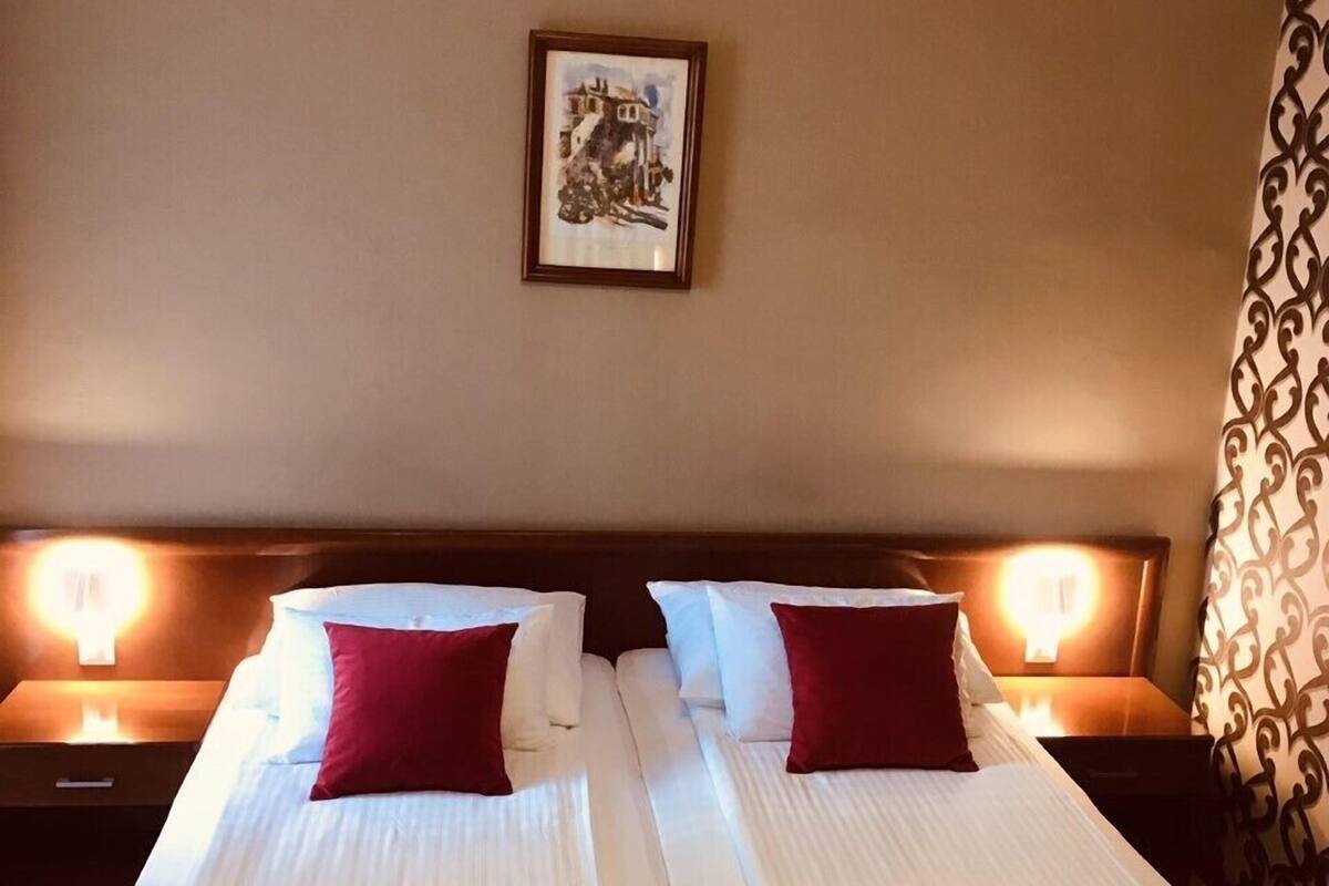 Een tweepersoonskamer met twee bedden, elk voorzien van een kussen en een opgevouwen handdoek. Aan de muur hangt een lijst met een foto en er is een kamerbreed gordijn met een patroon.